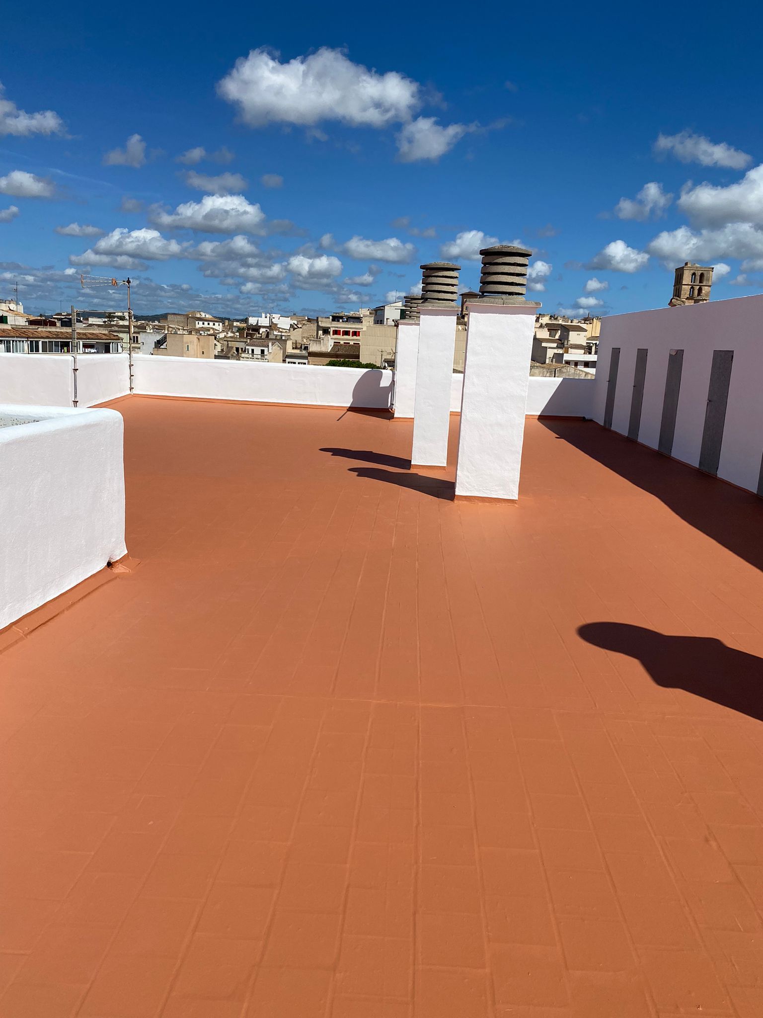 Teulada de terracota amb parets blanques i xemeneies contra un cel blau amb núvols.
