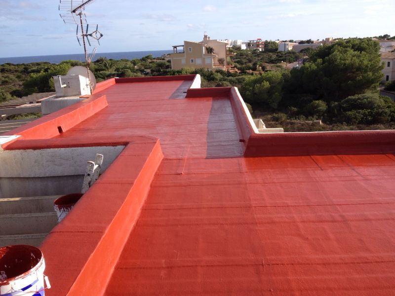 Teulada plana pintada de vermell d'un edifici amb vistes a la costa al fons.