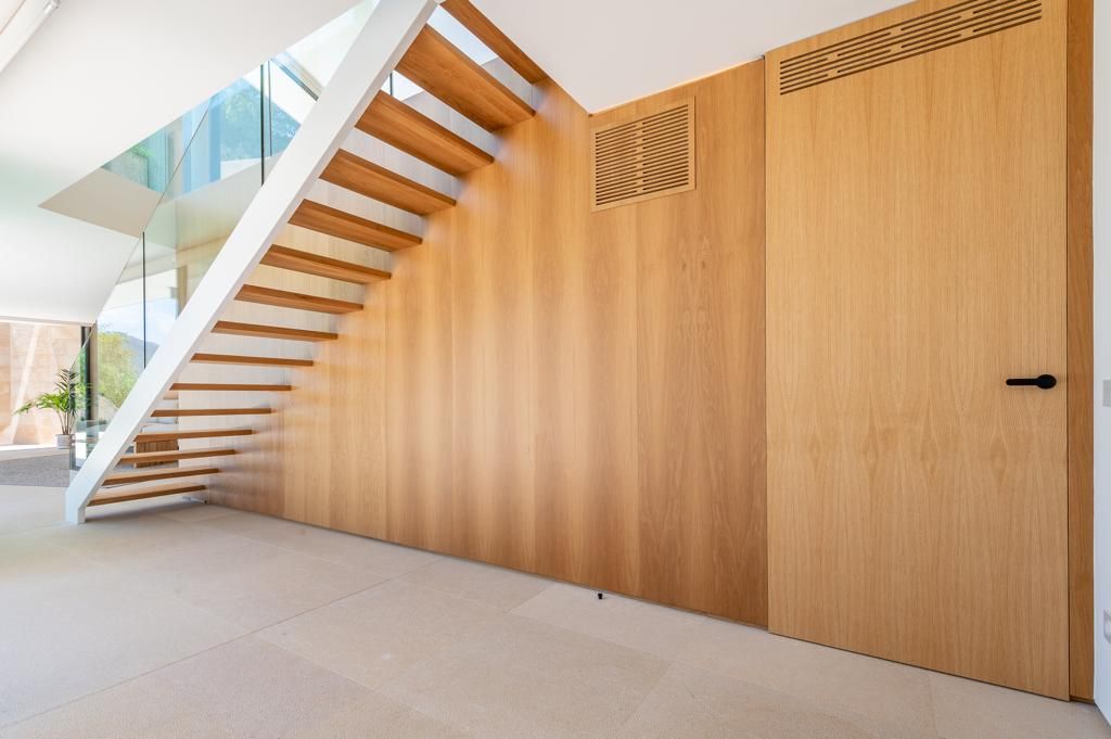 Escala de fusta amb barana blanca, paret de panells de fusta de color clar i porta.