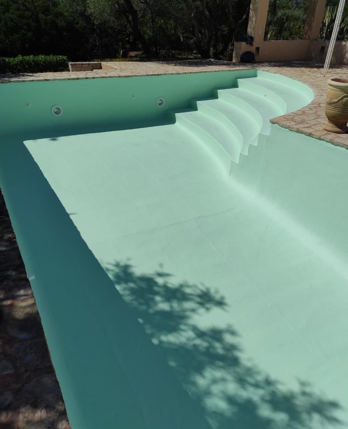 Piscina buida de color verd clar amb esglaons corbats i un entorn exterior assolellat.