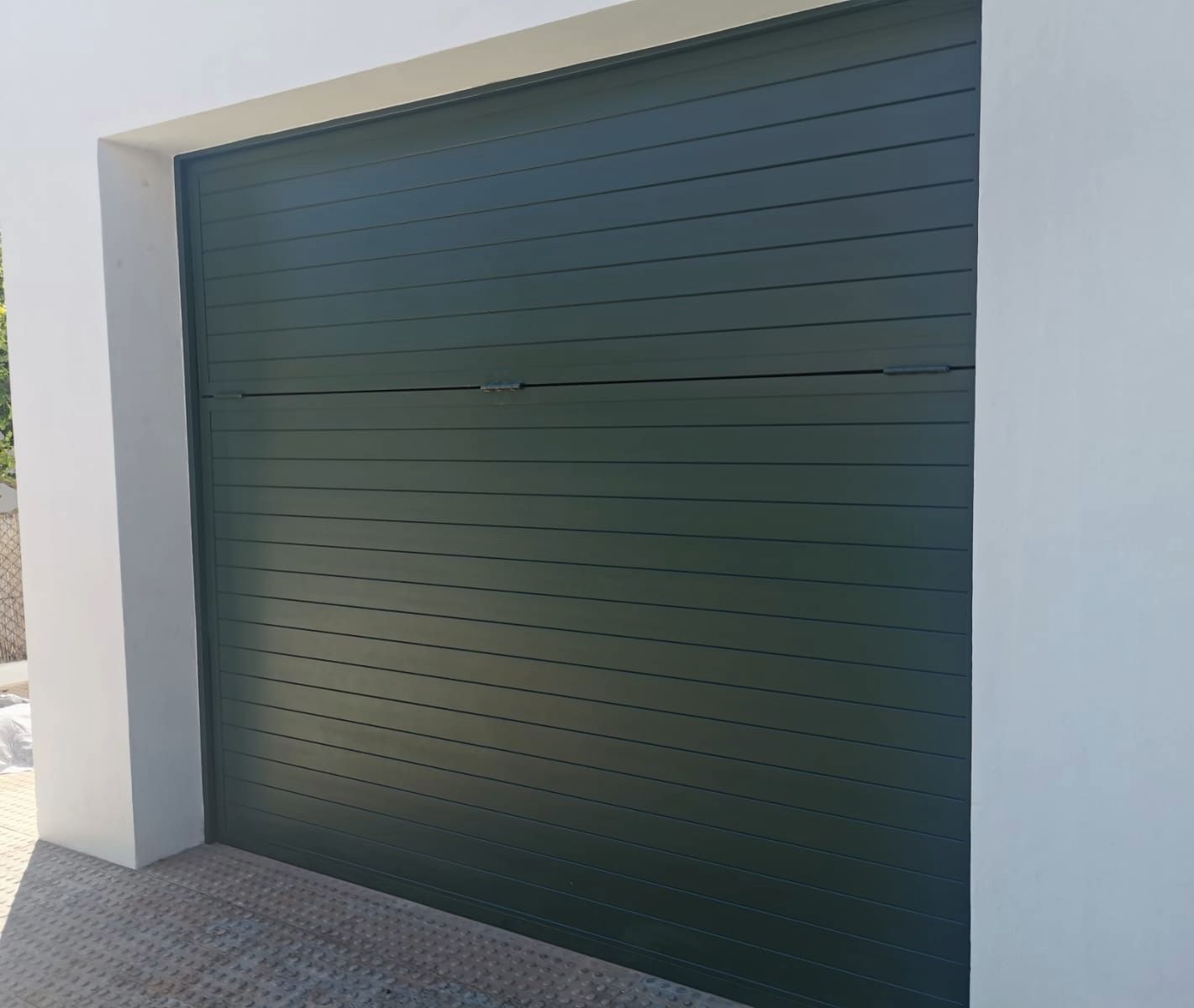 Porta de garatge de color verd fosc en un edifici blanc.