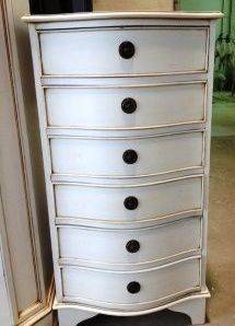 Còmoda blanca de sis calaixos amb fronts de calaix corbats i poms foscos.