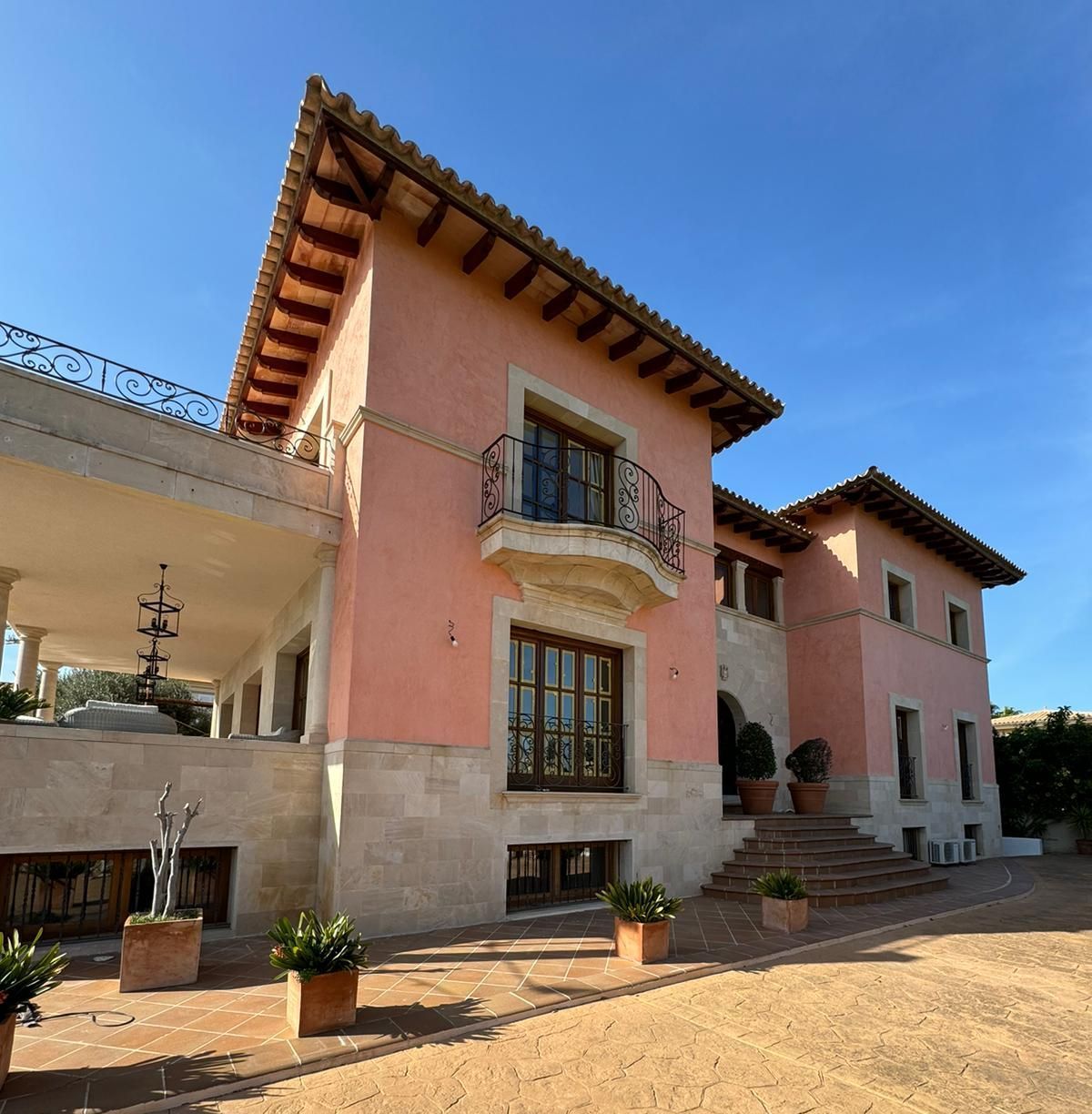 Mansió d'estuc rosa amb detalls de pedra, teules de terracota i un balcó de ferro forjat ornamentat.