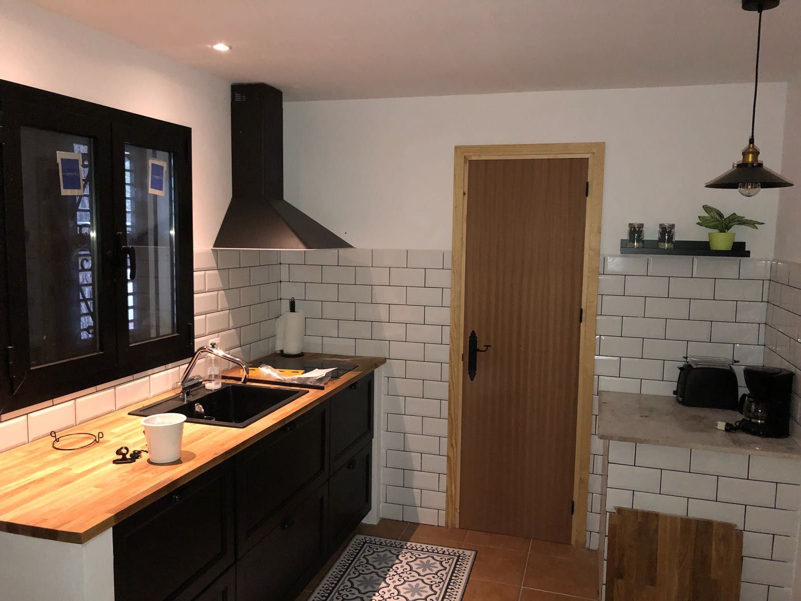 Una cocina con gabinetes negros y azulejos blancos tiene una puerta de madera.