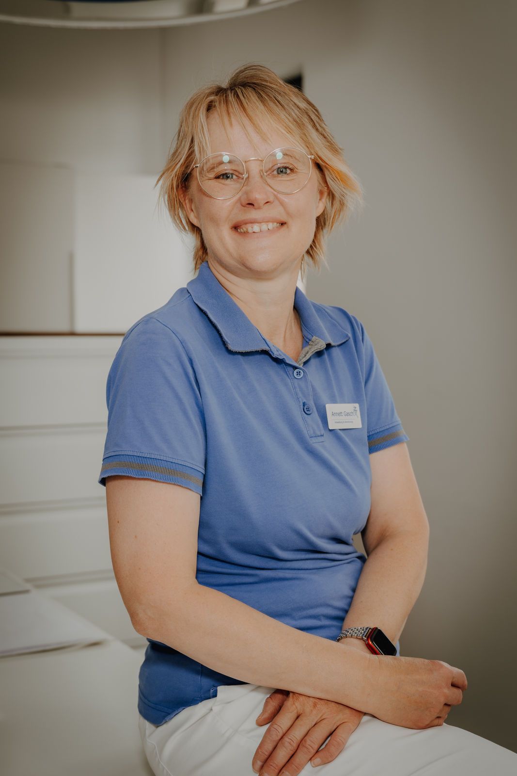 Eine Frau in einem blauen Poloshirt lächelt, sie sitzt in einem hellen Arztzimmer.