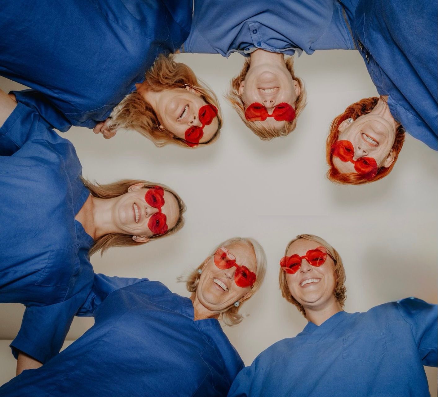 Zwei Personen in blauer OP-Kleidung lehnen lächelnd an einer blauen Säule im Flur einer Arztpraxis.