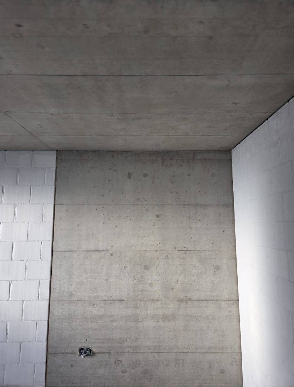 Unfertige Betonwand und -decke in einem kleinen Raum mit weißen Betonsteinwänden an den Seiten.