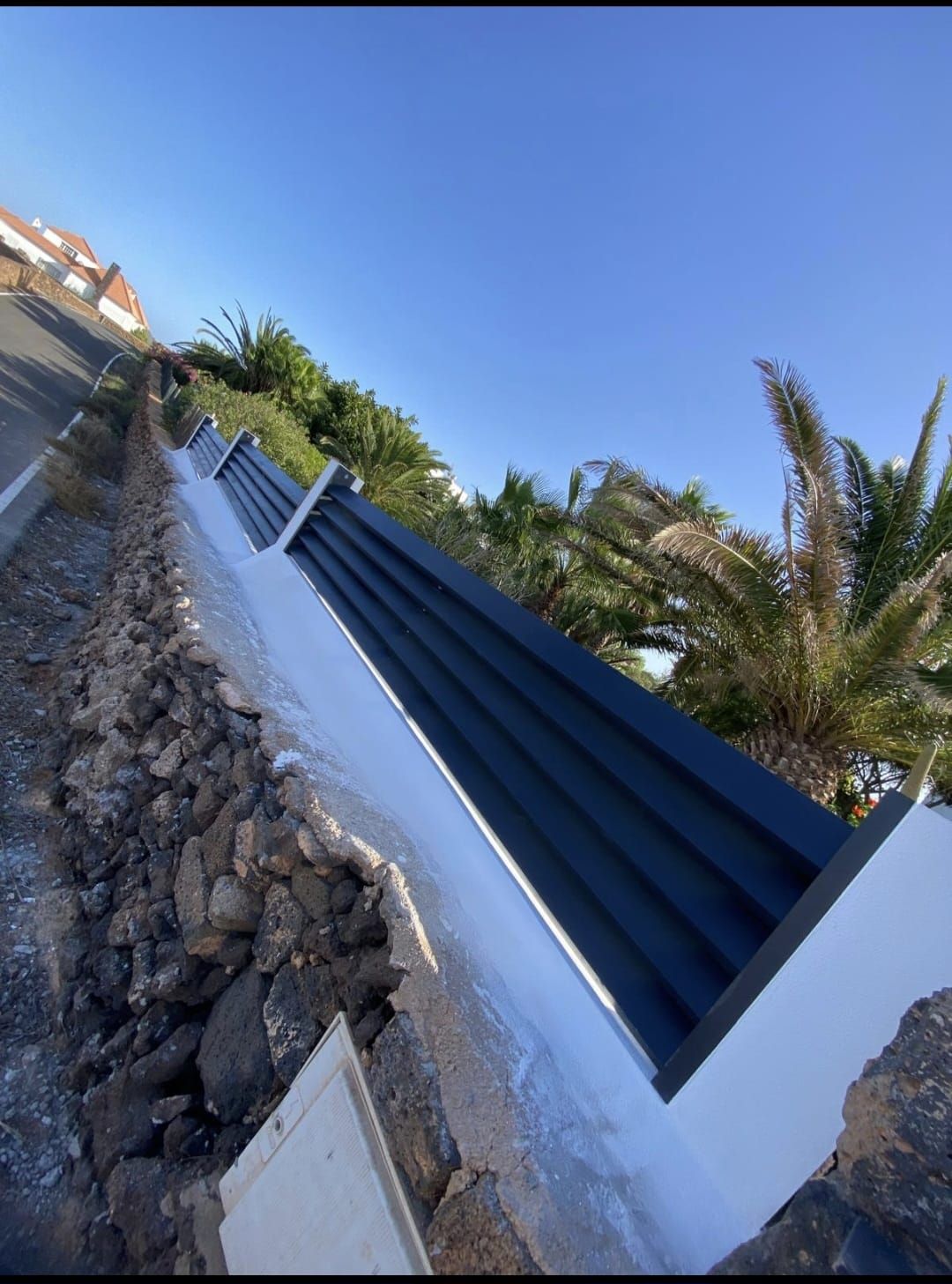 Una valla negra rodea un muro de piedra junto a una carretera