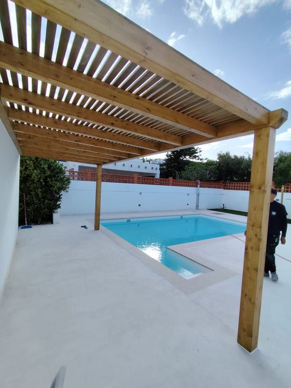 Un hombre se encuentra bajo una pérgola de madera sobre una piscina.