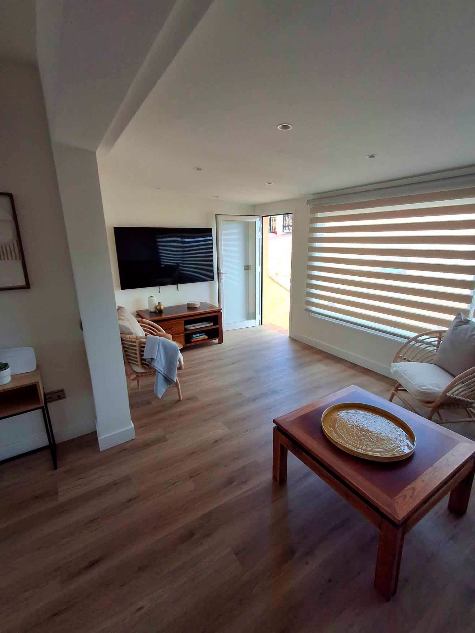 Una sala de estar con pisos de madera, una mesa de café, sillas y un televisor de pantalla plana.