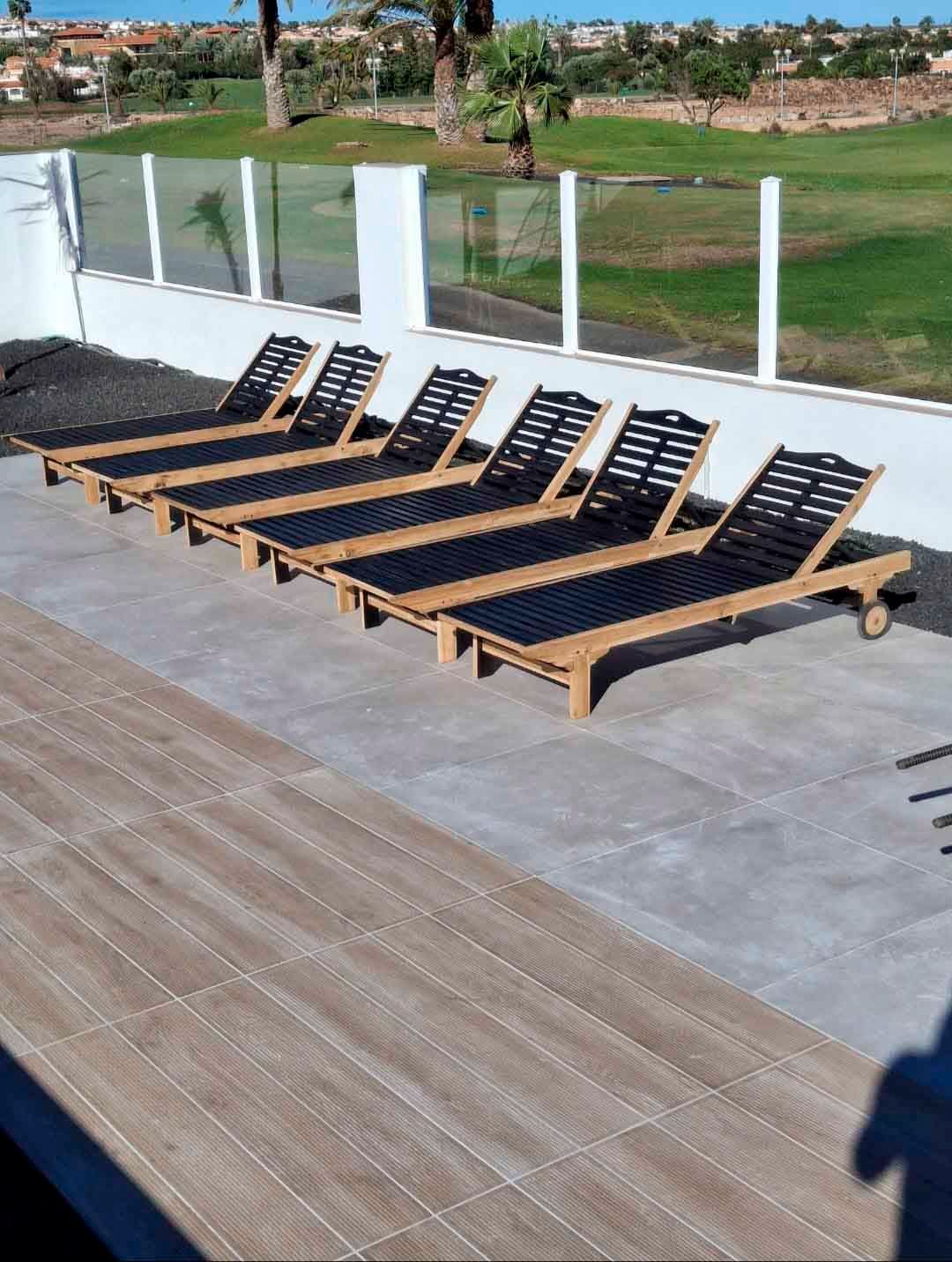 Una fila de tumbonas están alineadas en un patio al lado de un campo de golf.
