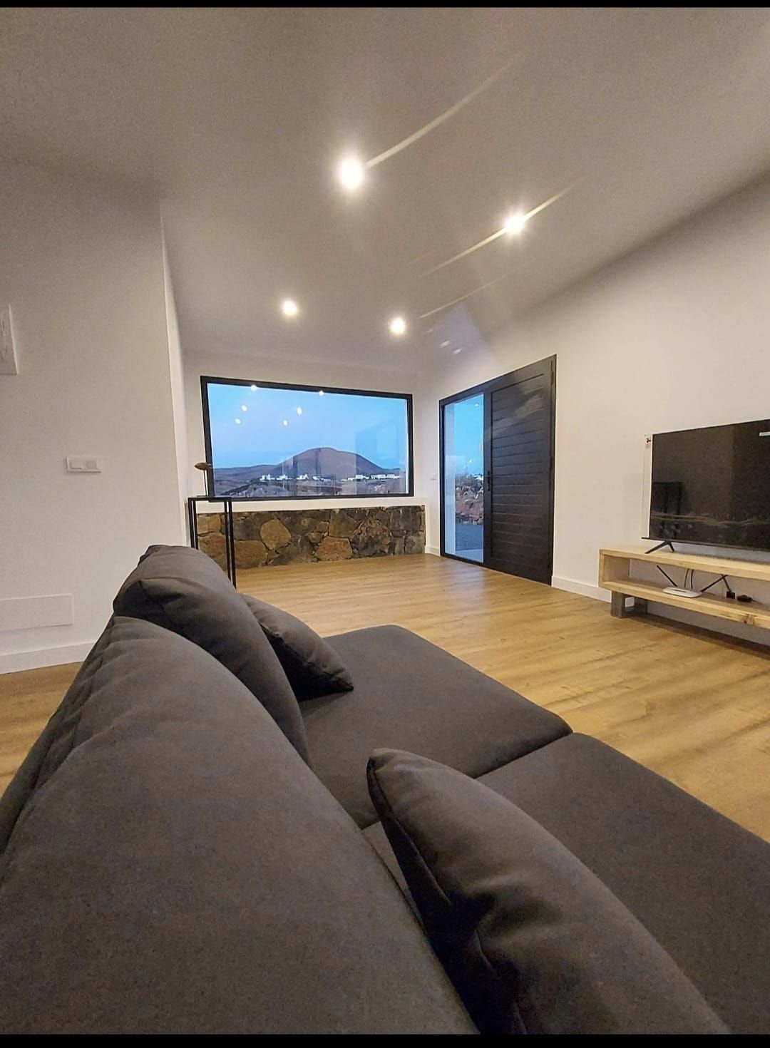 Una sala de estar con sofá, televisión y una ventana grande.