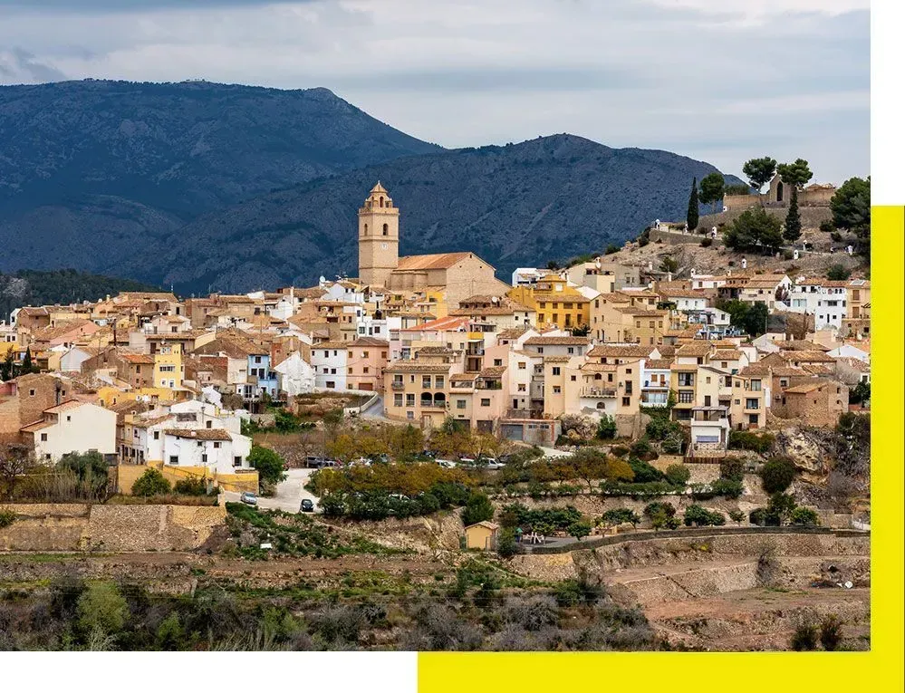 Una camioneta blanca está estacionada frente a un avión que vuela en el cielo.
