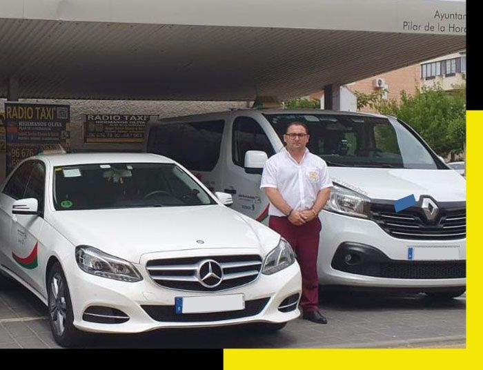Un hombre se encuentra de pie entre un Mercedes blanco y una furgoneta Renault blanca en un aparcamiento.