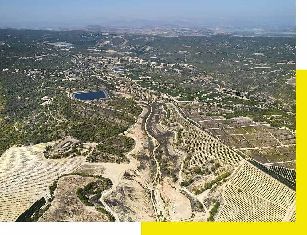 Una camioneta blanca está estacionada frente a un avión que vuela en el cielo.