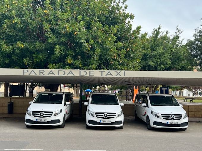 Tres camionetas blancas están estacionadas frente a un edificio que dice parada de taxi.