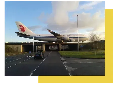 Una camioneta blanca está estacionada frente a un avión que vuela en el cielo.