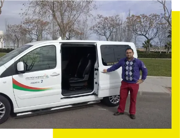 A person standing beside a white passenger van with the side door open, parked in a park setting.