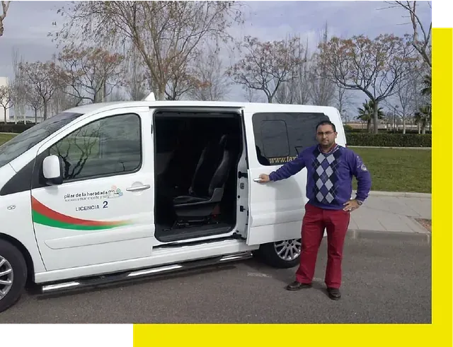 A person standing beside a white passenger van with the side door open, parked in a park setting.