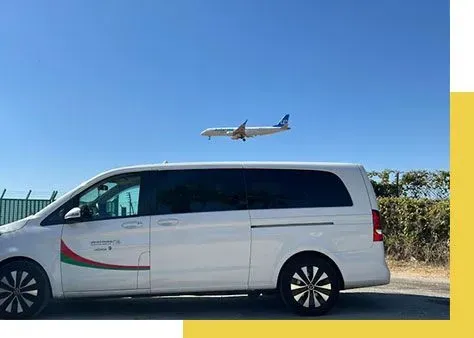 Una camioneta blanca está estacionada frente a un avión que vuela en el cielo.