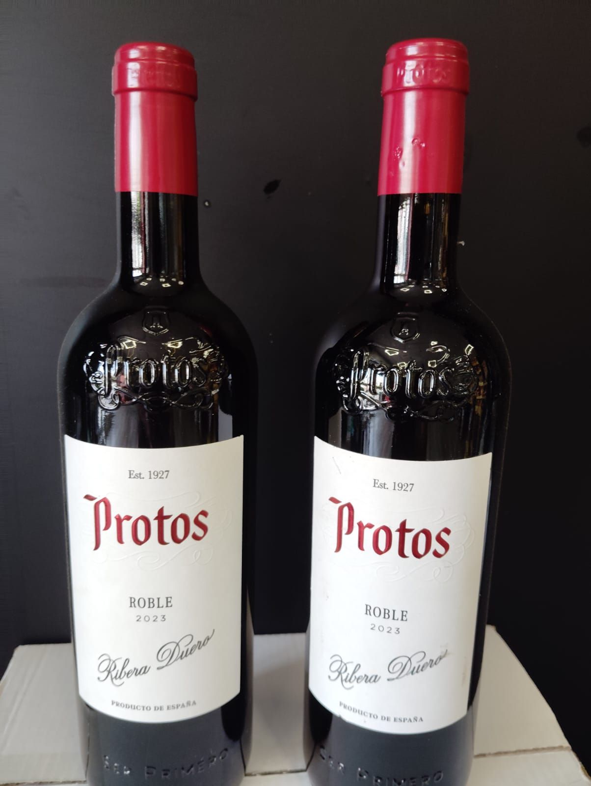 Dos botellas de vino protos con tapones rojos.