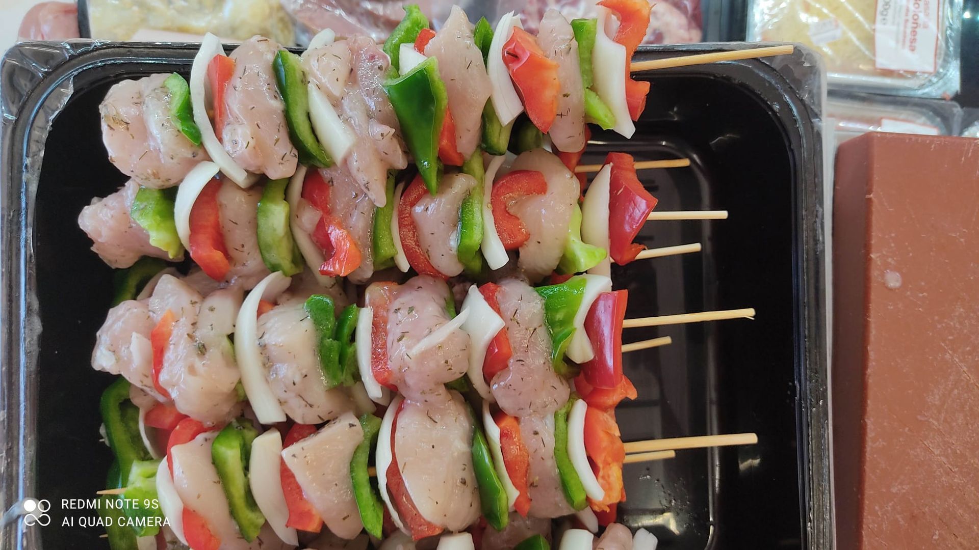 Un recipiente de plástico lleno de brochetas de carne y verduras.