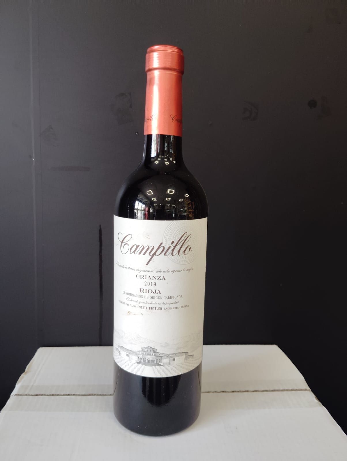 Una botella de vino Campillo reposa sobre una caja blanca.
