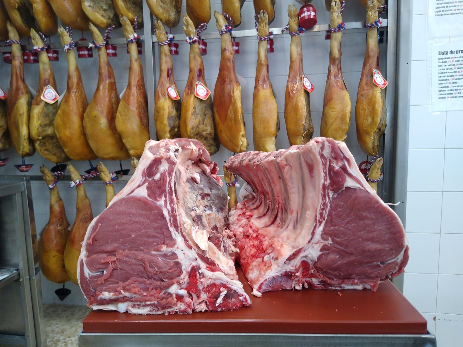 Dos trozos de carne están sobre una mesa delante de una pared de jamones.