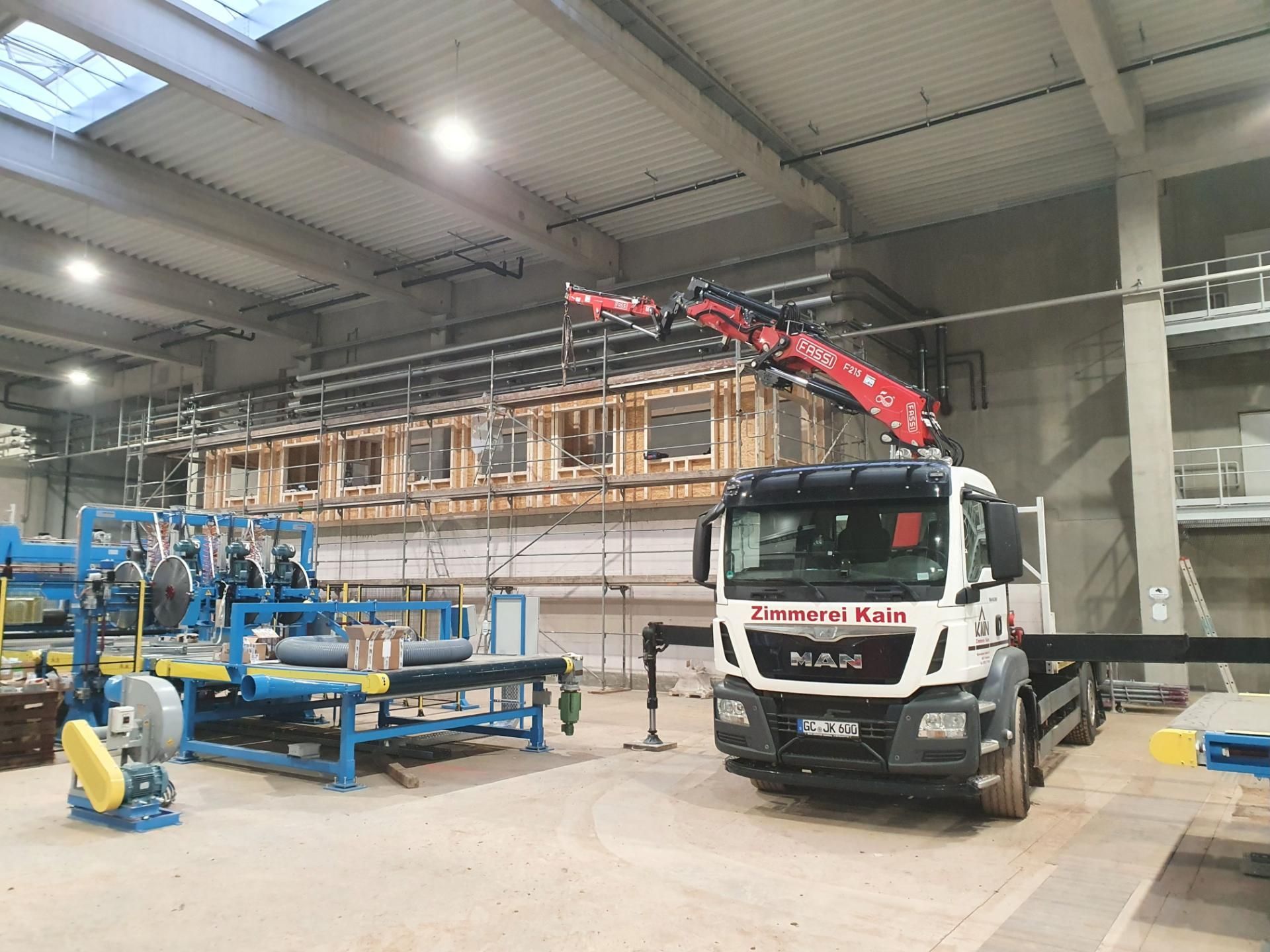 Holzrahmenkonstruktion eines Gebäudes in einer Halle, davor ein LKW mit Kran der Zimmerei Kain