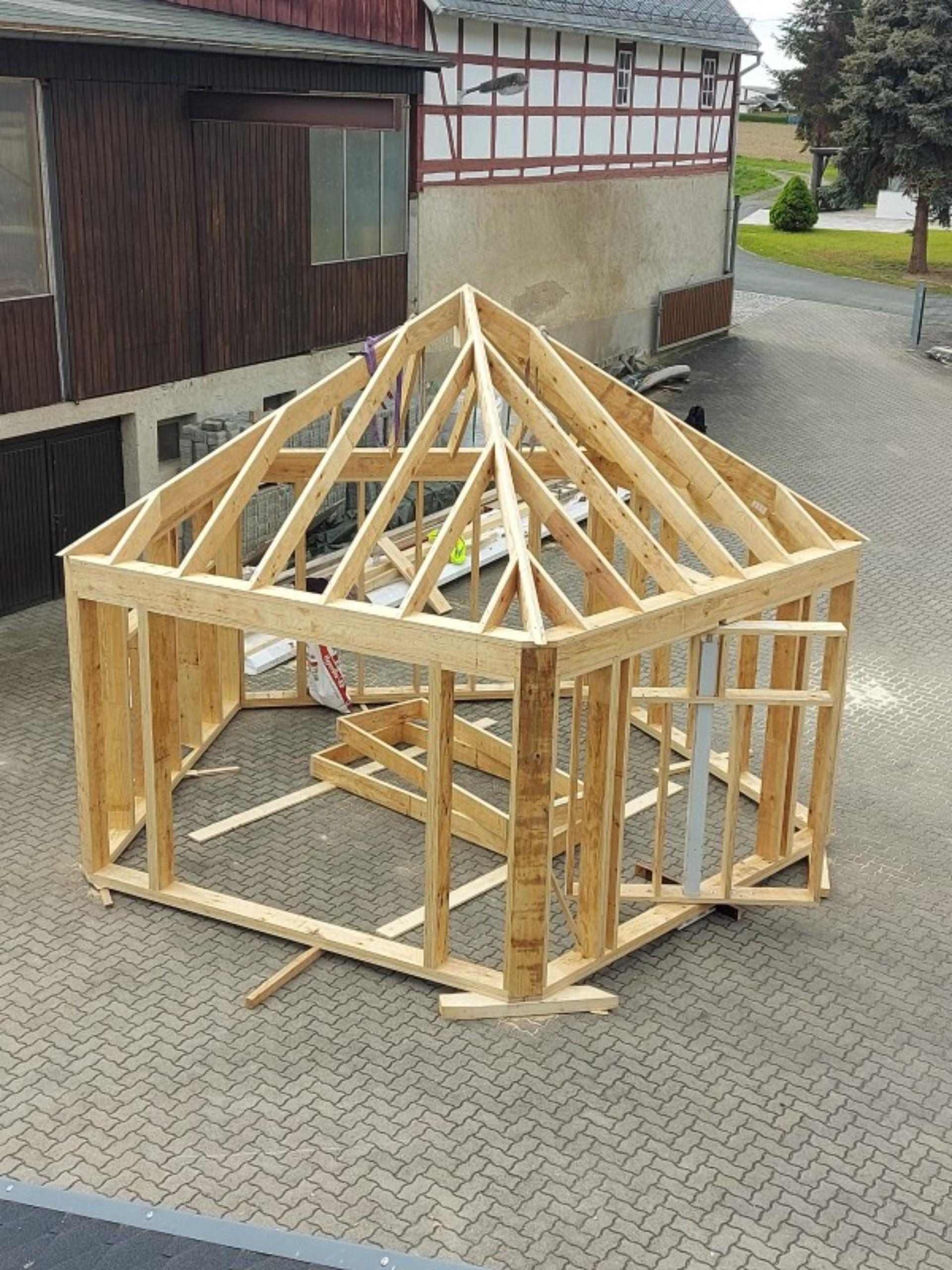 Holzrahmenkonstruktion eines achteckigen Pavillons im Bau auf gepflastertem Hof vor Fachwerkhaus