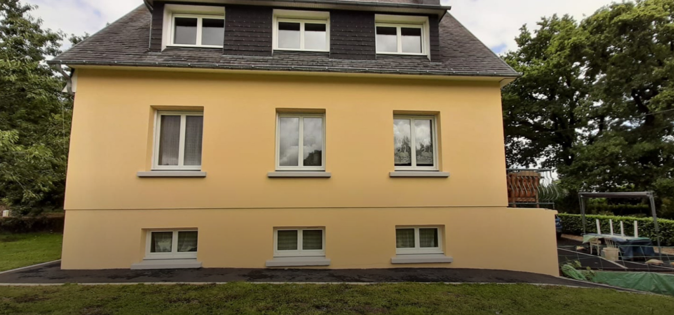 Maison jaune à deux étages avec toit foncé et fenêtres à encadrement blanc, vue de face.