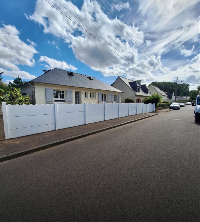 Rue résidentielle tranquille avec des maisons blanches, une clôture blanche et un ciel bleu nuageux.