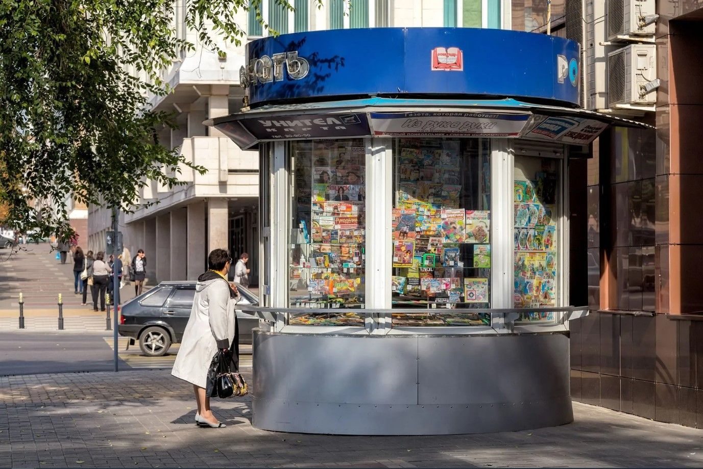 Quiosco en una acera de la ciudad; persona mira los artículos en venta; día soleado.