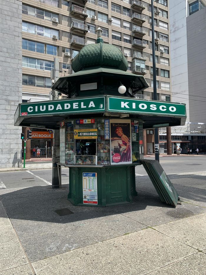 Mujer hojeando libros en una mesa, librería con estantes, hombre detrás del mostrador, ventana grande.