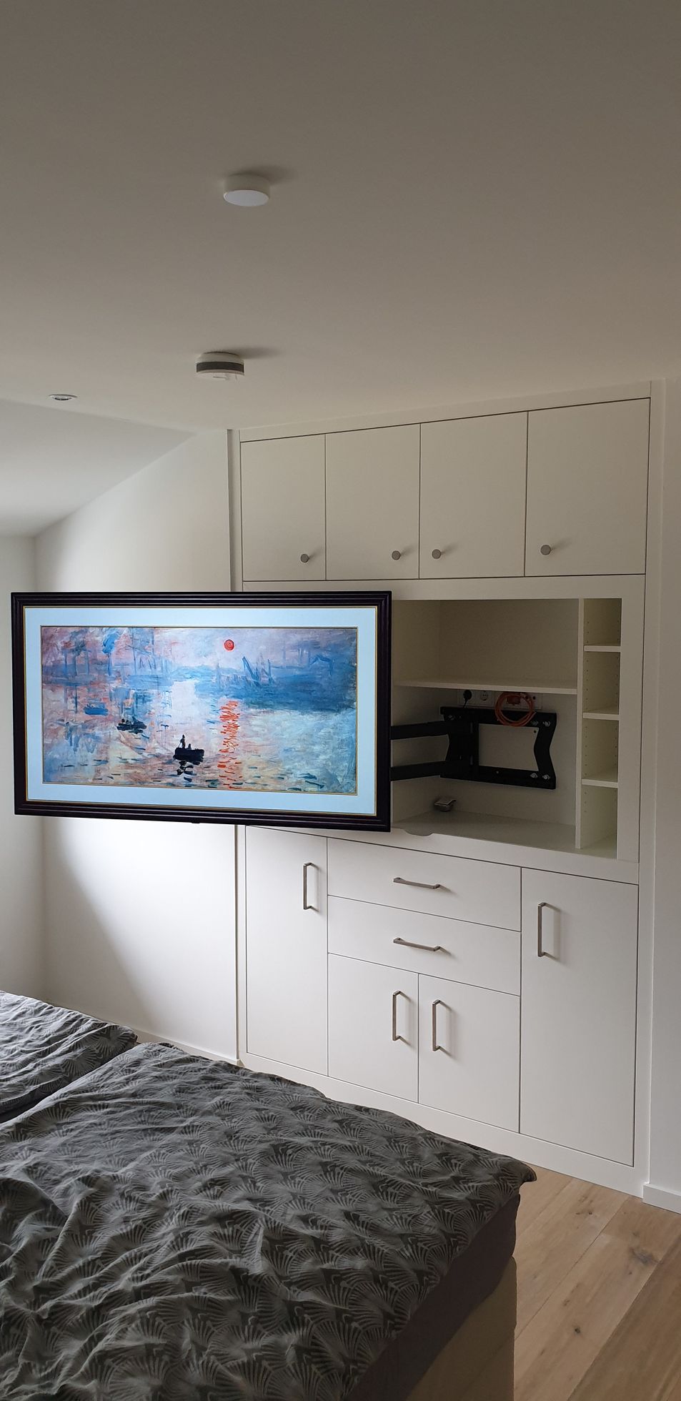 Ein Schlafzimmer mit einem Flachbildfernseher, der an der Wand über einem Bett montiert ist.