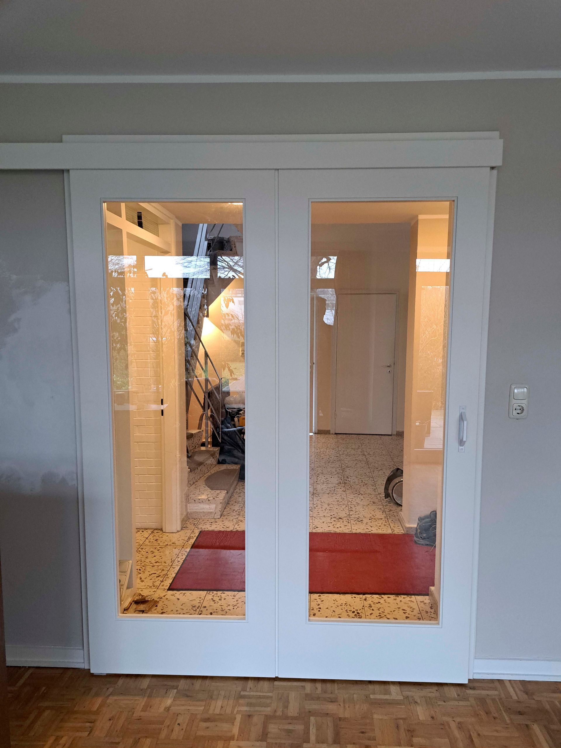 Ein Wohnzimmer mit einer Glasschiebetür, die zu einem Flur führt.