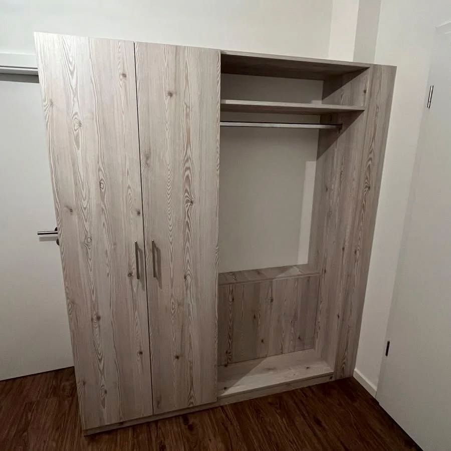 In einem Raum neben einer Tür steht ein großer Holzschrank.