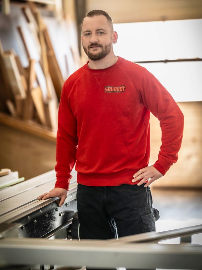 Ein Mann in einem roten Pullover steht vor einer Tischkreissäge.