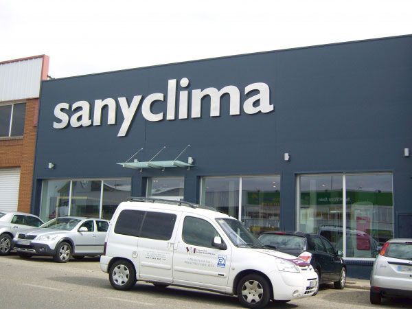 Una camioneta blanca está estacionada frente a un edificio que dice sanyclima