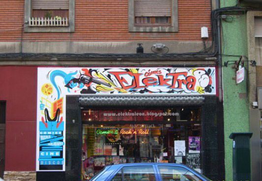 Un coche azul está aparcado delante de una tienda con un grafiti.