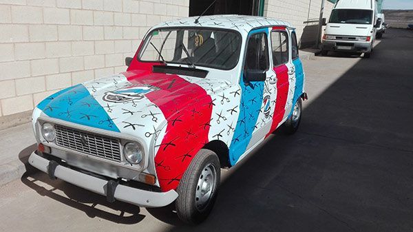 Un coche rojo, blanco y azul está aparcado delante de un edificio de ladrillos.