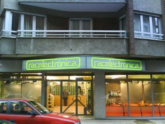 Un coche rojo está aparcado delante de una tienda de electrónica de carreras.