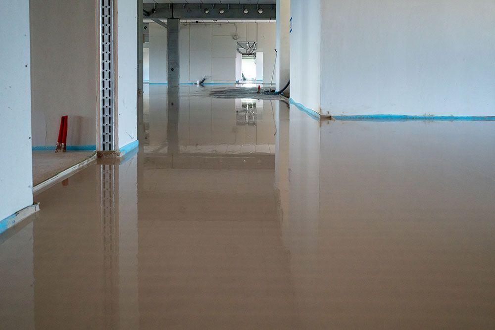 Innenansicht eines im Bau befindlichen Gebäudes mit einem glatten, braunen, frisch verlegten Fußboden. Die Wände sind weiß.