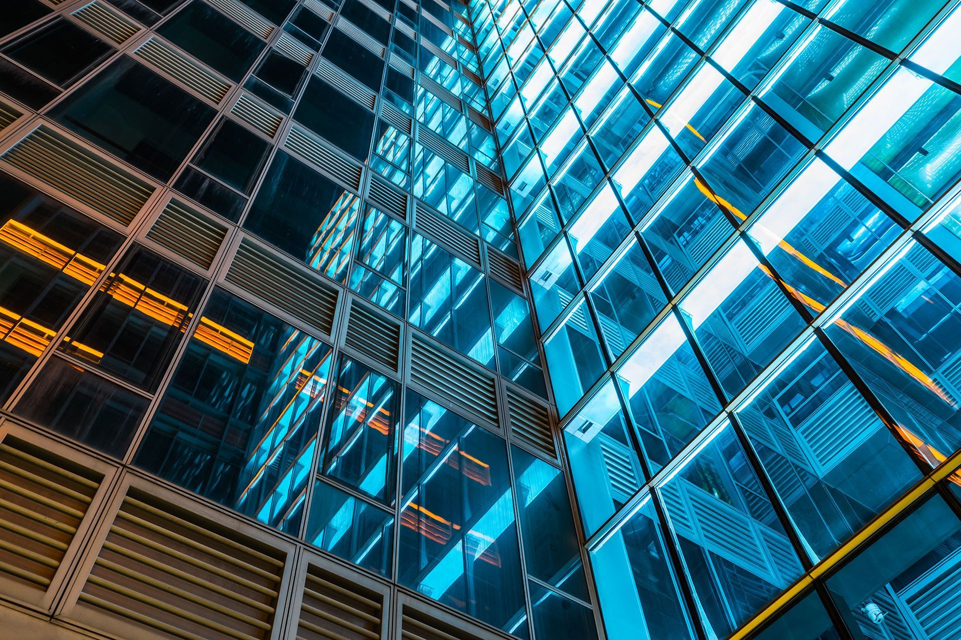 Blauer Glaswolkenkratzer, schräge Ansicht, Spiegelungen des Himmels und der Gebäudeelemente.
