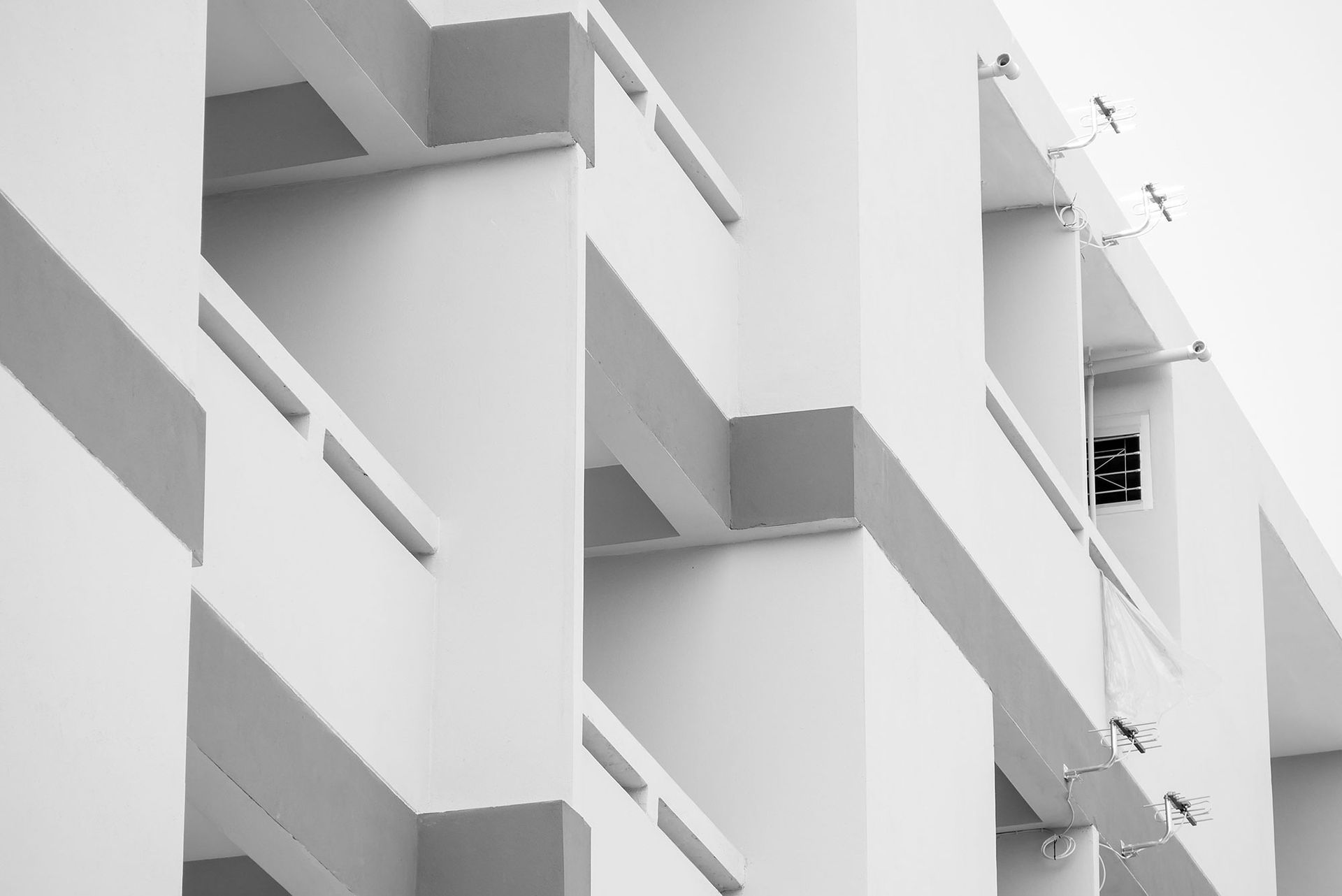 Schwarz-Weiß-Fotografie einer Gebäudefassade mit geometrischen Formen, Fenstern und Schatten.