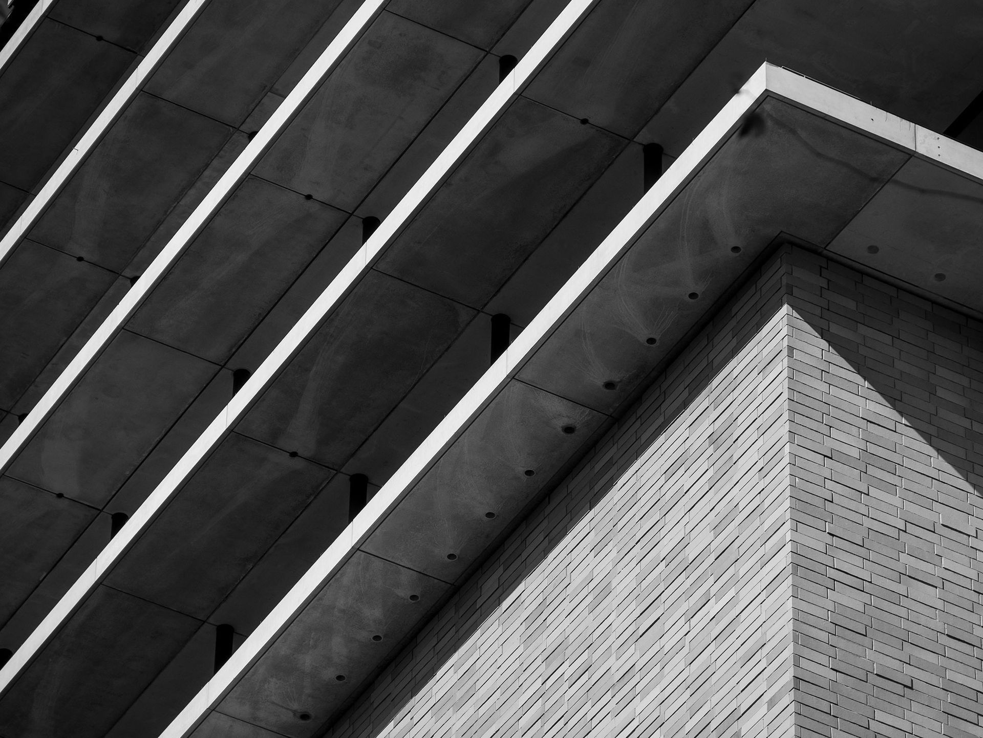 Architekturaufnahme in Schwarz-Weiß von einem Gebäude mit schrägen Betonvorsprüngen und einer Ziegelecke.