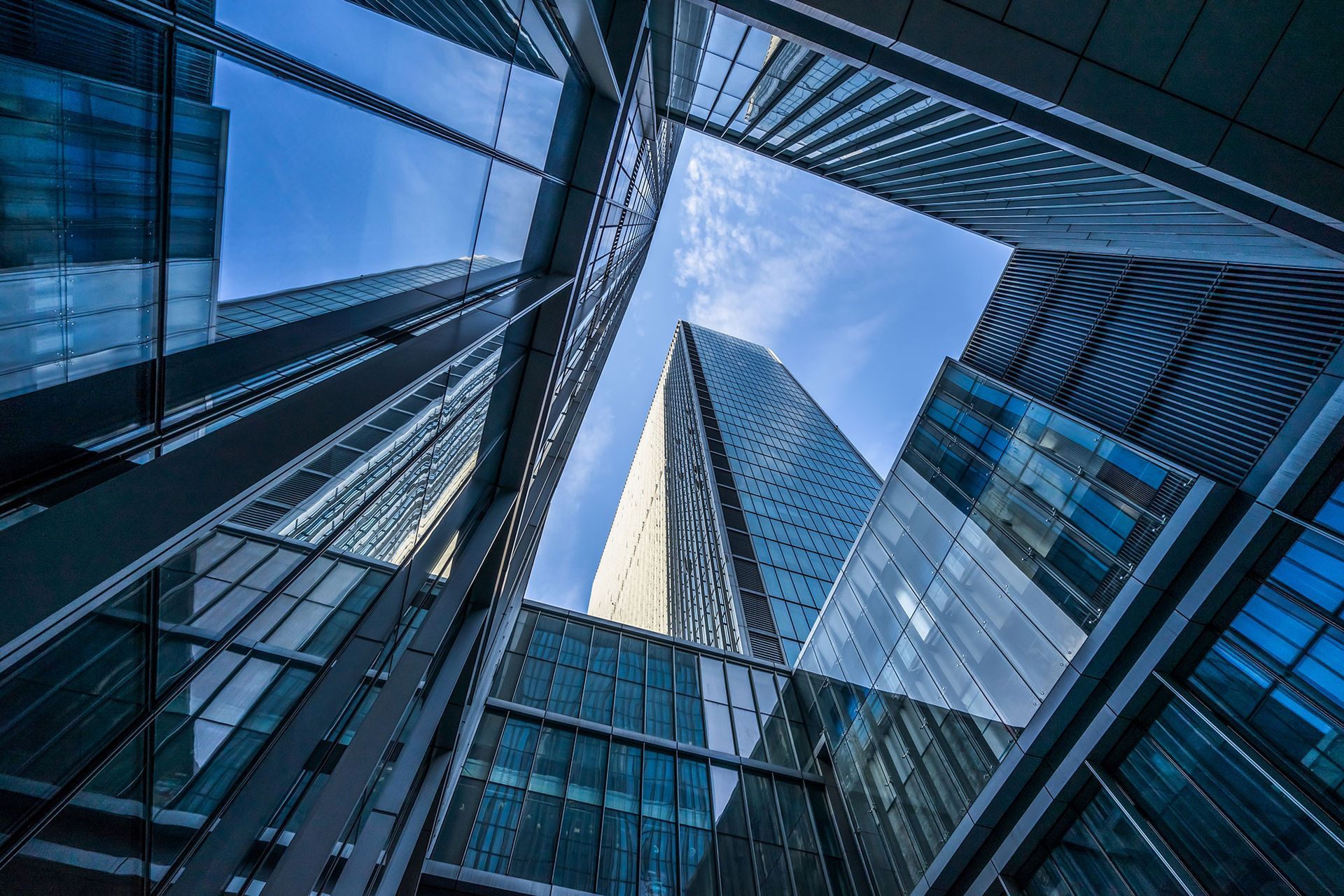 Ansicht von unten auf hohe, moderne Wolkenkratzer mit spiegelnden Glasfassaden vor blauem Himmel.