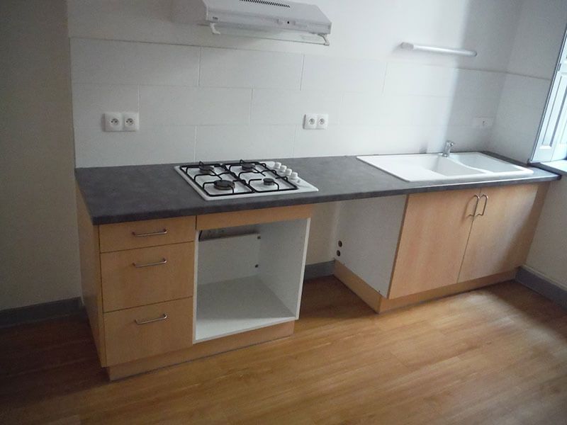 Petit comptoir de cuisine avec cuisinière à gaz, évier, placards et carrelage blanc dans une pièce lumineuse