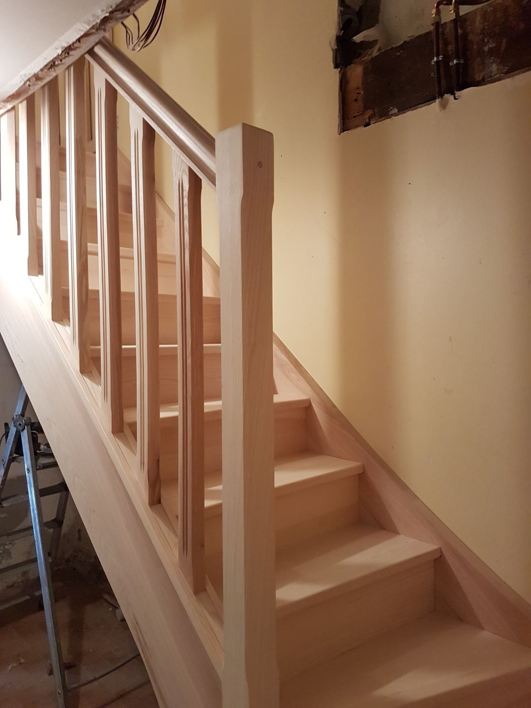 Escalier intérieur avec marches en bois clair et rampes blanches le long d'un mur beige.