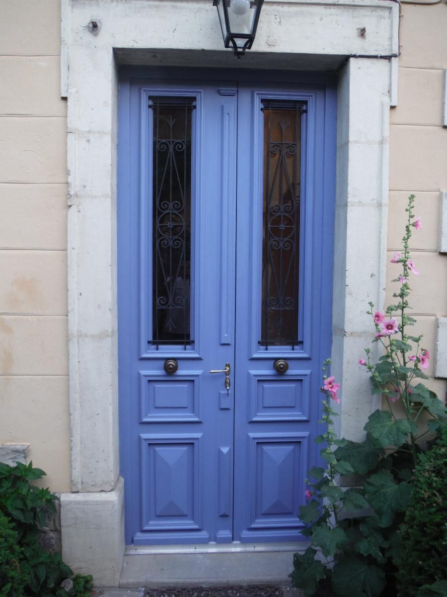 Porte d'entrée double bleue avec d'étroits panneaux de verre et des fleurs roses à côté.